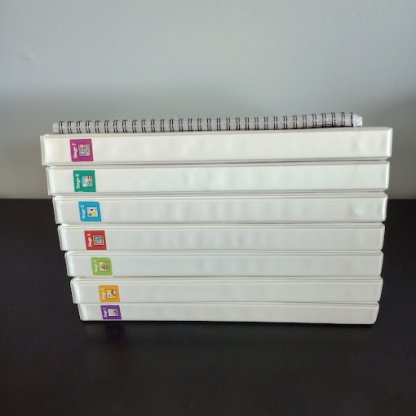 Seven white half-inch binders stacked on top of one another