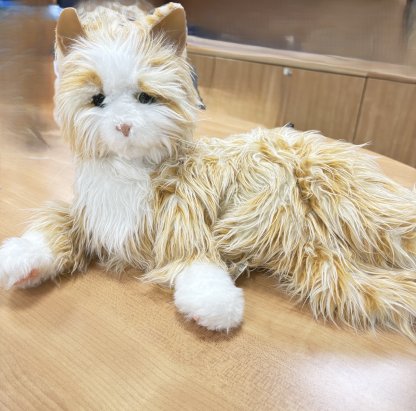 Orange tabby cat robotic animal laying down with its eyes open. 