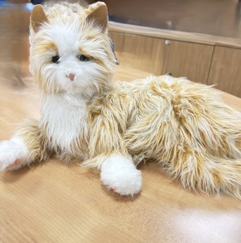 Orange tabby cat robotic animal laying down with its eyes open. 
